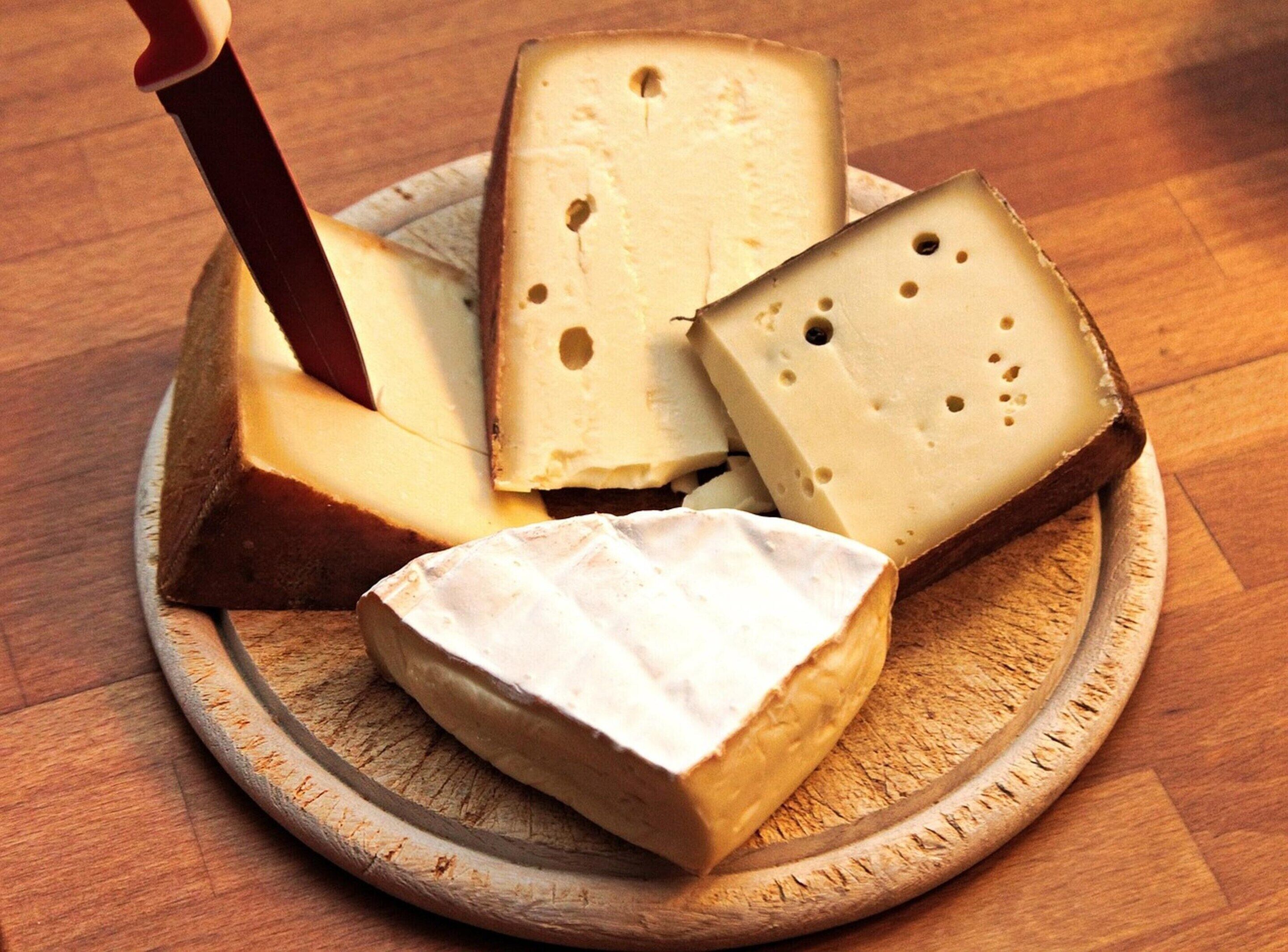 Una tabla de madera redonda con varios trozos de queso, incluyendo un trozo con un cuchillo insertado.