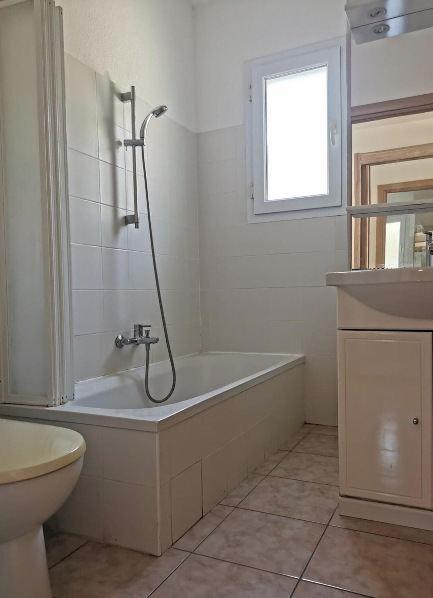 A bathroom with a bathtub, toilet, and a window.