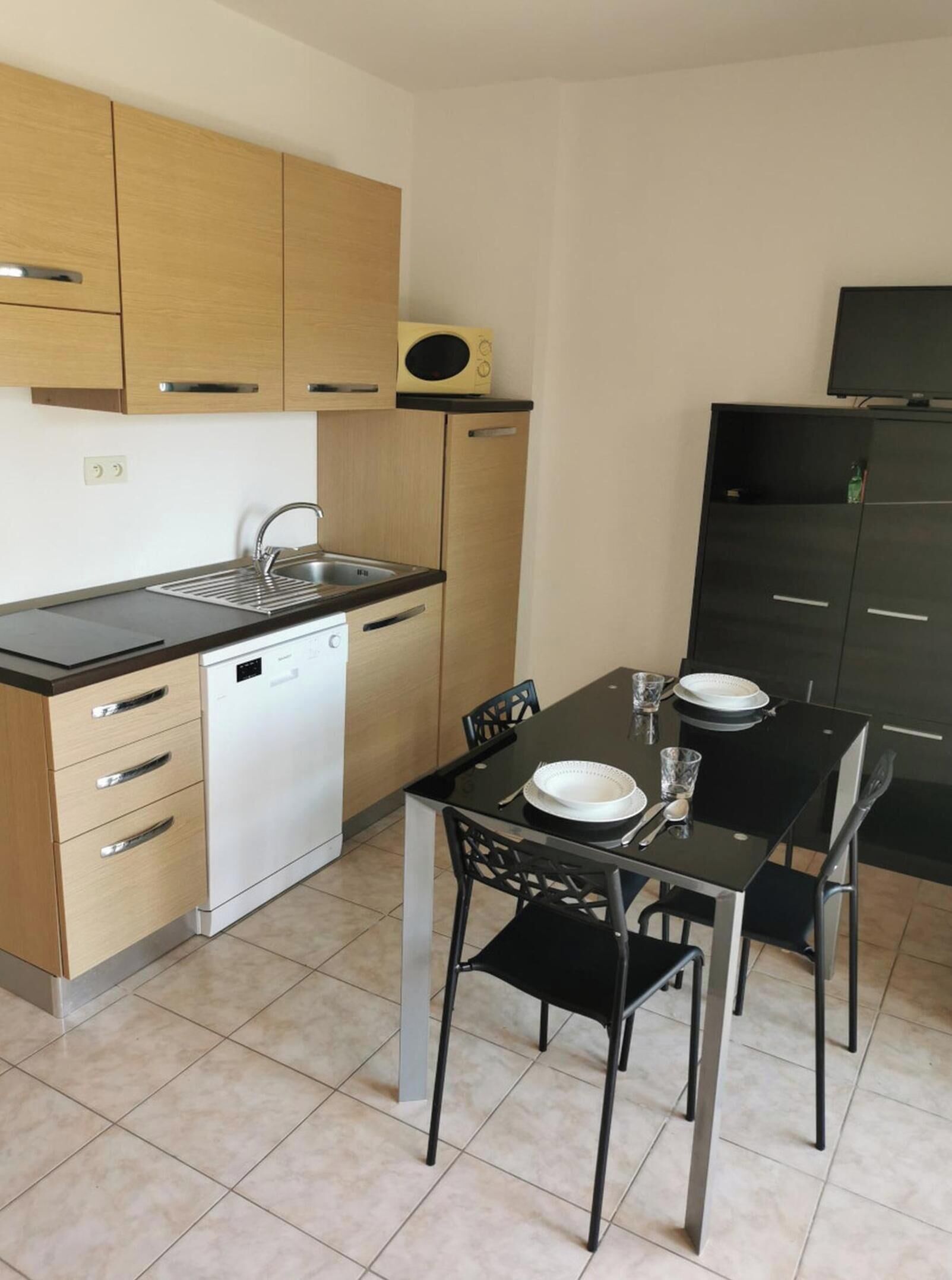 Una cocina compacta con lavavajillas, microondas, una mesa de comedor con sillas y un armario negro.