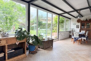 Ein geräumiges Zimmer mit großen Fenstern, einem Holztisch, Stühlen und einem Schrank.