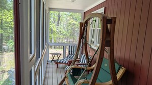 A covered porch with wooden swing chairs and a table. - Charming Home Near Lake Winnipesaukee Beach Access 3 Bedroom Home (Moultonborough)