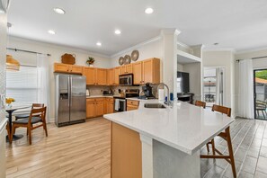 A modern kitchen with wooden cabinets, stainless steel appliances, and a central island. - Serene Villa with Heated Pool & Arcade Near Disney (Clermont)
