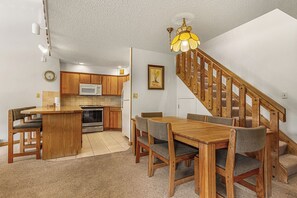 A kitchen with wooden cabinets, a microwave, an oven, and a dining area with a wooden table and chairs. - Ski-In Condo | Loft + Fireplace | Near Main St (Breckenridge)