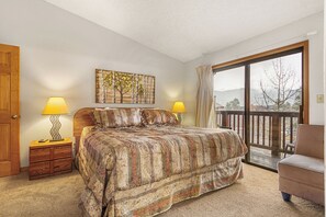 A bedroom with a large bed, two bedside lamps, a wooden headboard, a painting on the wall, and a balcony with a view. - Ski-In Condo | Loft + Fireplace | Near Main St (Breckenridge)