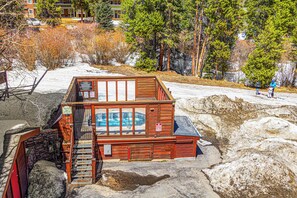 A wooden cabin with a hot tub, a staircase, and a view of a snowy landscape. - Ski-In Condo | Loft + Fireplace | Near Main St (Breckenridge)