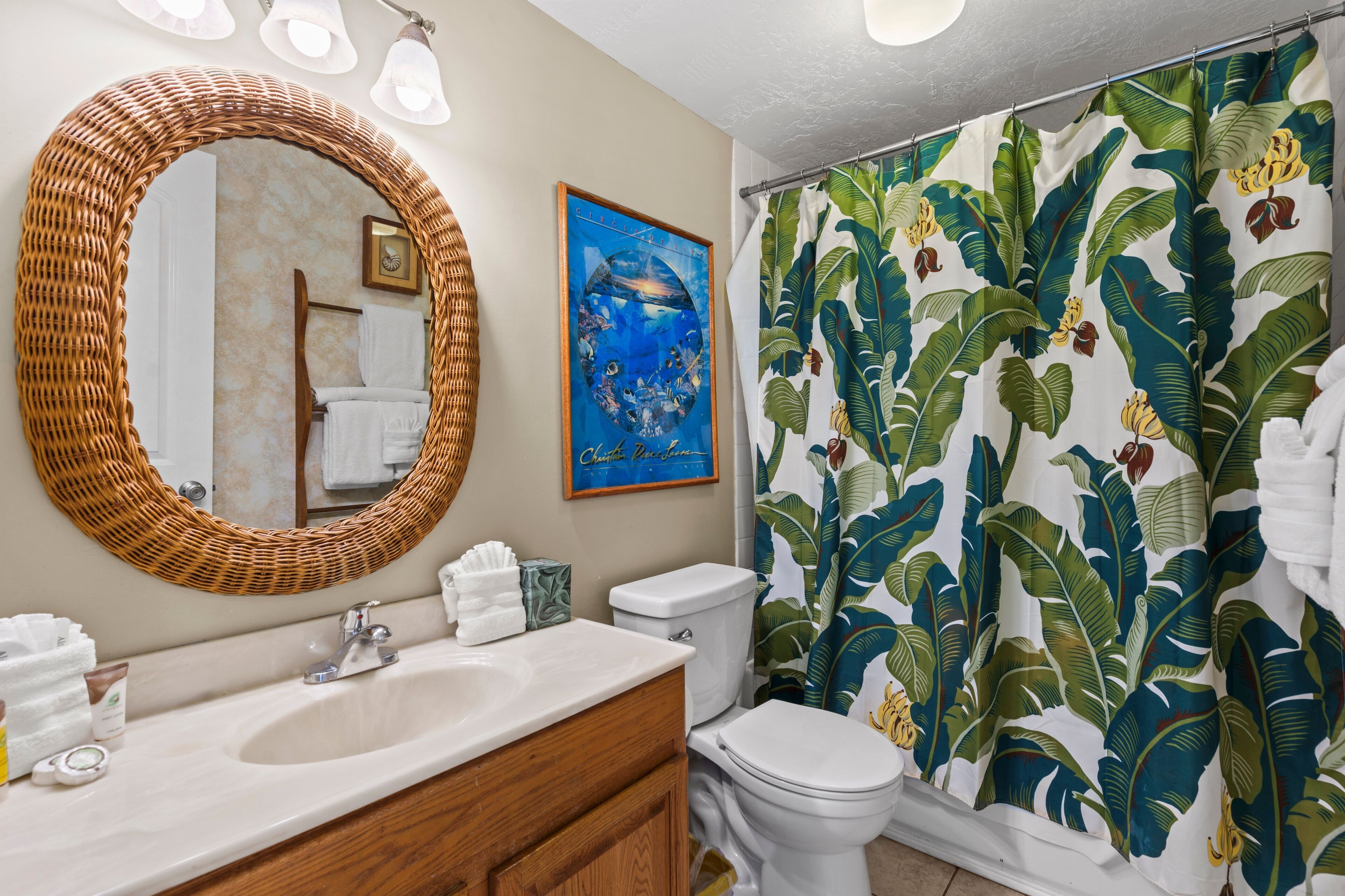 A bathroom with a large mirror, a sink, a toilet, and a shower curtain with a tropical leaf pattern.
