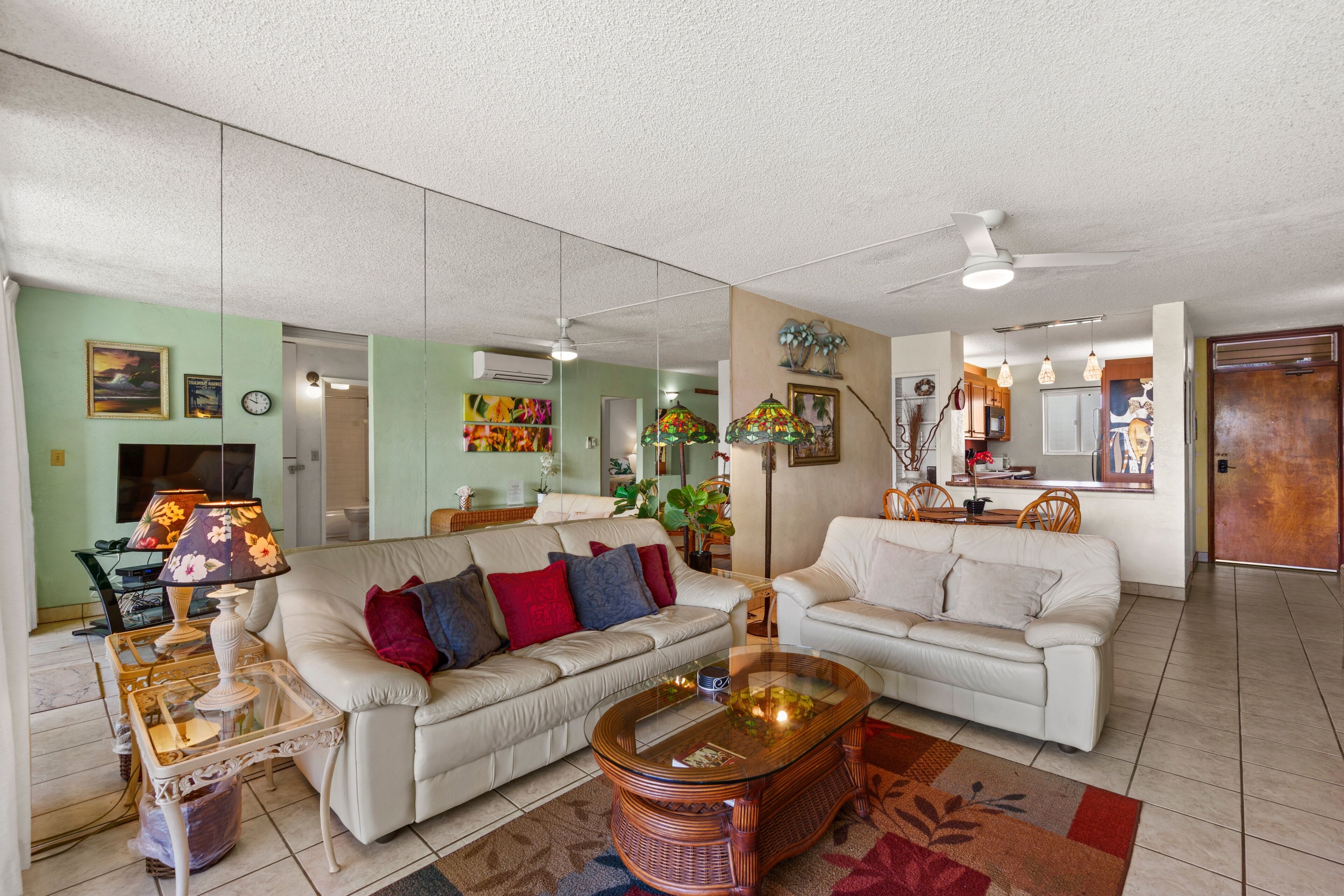 A spacious living room with two white sofas, a glass coffee table, and a dining area with wooden chairs.
