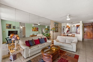 A spacious living room with two white sofas, a glass coffee table, and a dining area with wooden chairs.