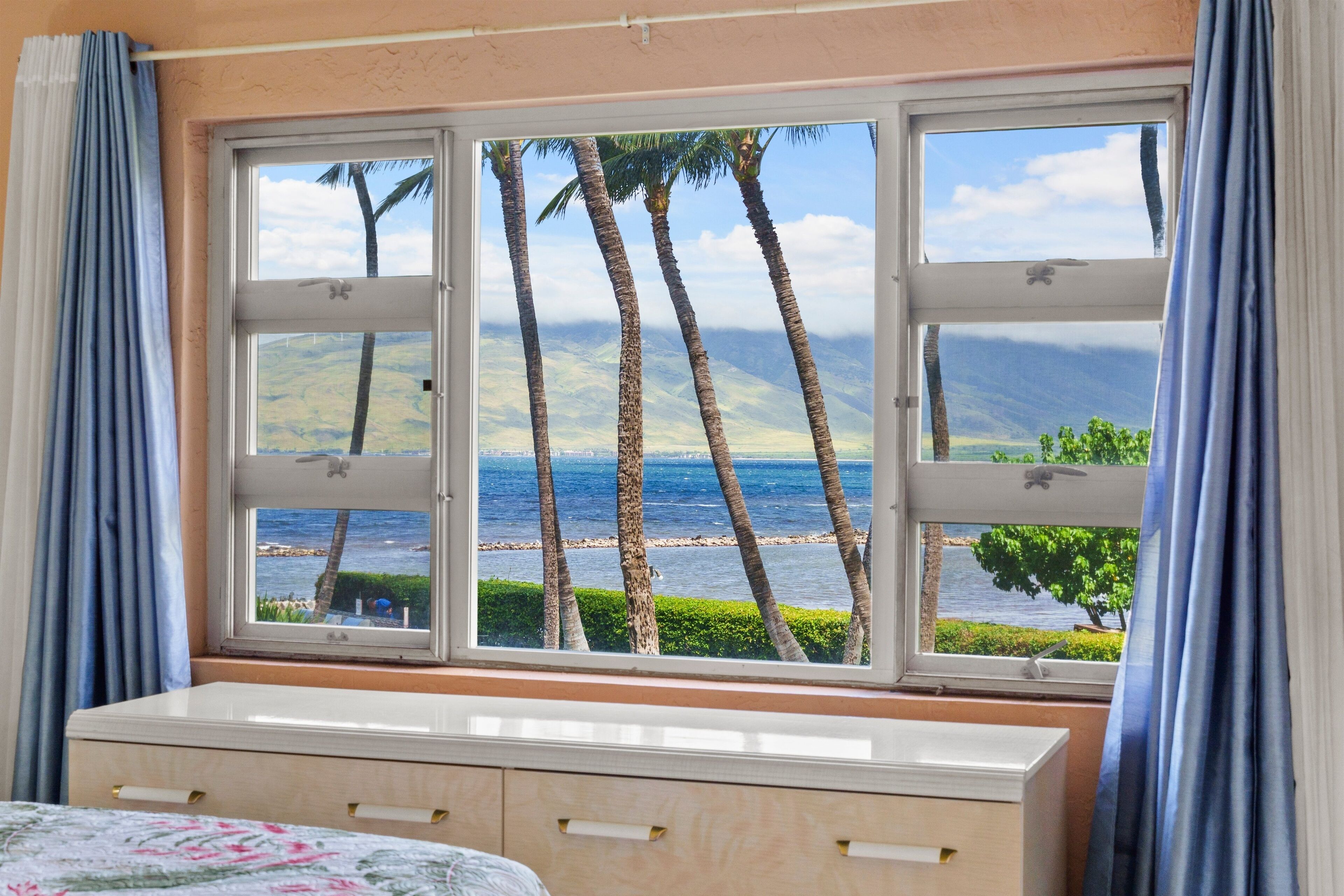 A room with a large window overlooking a beach with palm trees and a view of the ocean.