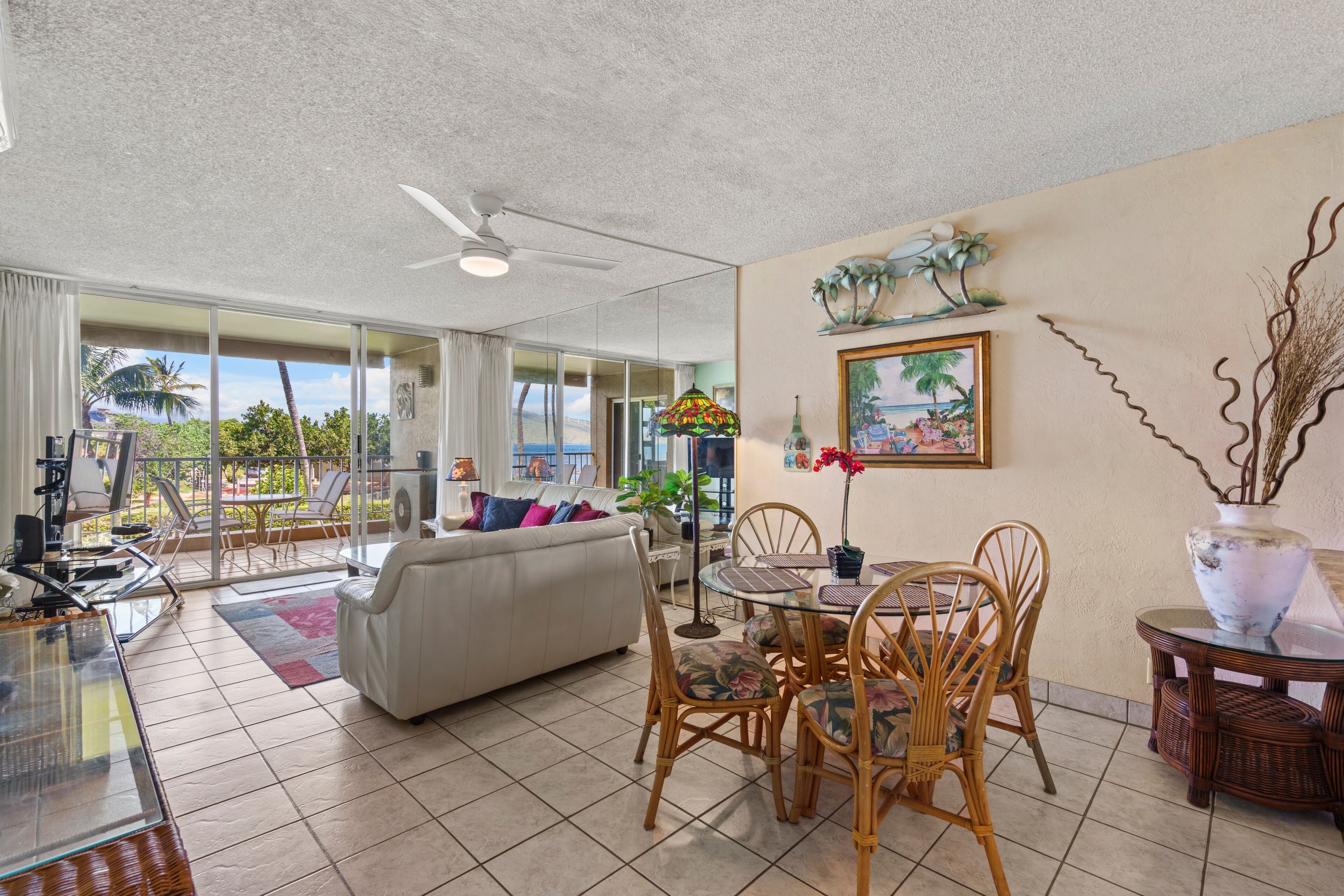 A spacious living area with a sofa, dining table, and chairs, a ceiling fan, and a view through large glass doors to the outdoors.