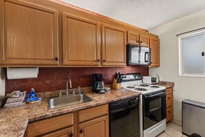 A kitchen with wooden cabinets, a stainless steel sink, a microwave, a coffee maker, a toaster, and a stove. - Menehune Shores, #206 2 Bedroom Condo (Kihei)
