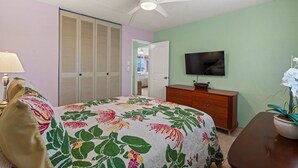 Ein Schlafzimmer mit einem Bett, einem Schminktisch, einem Fernseher und einem Deckenventilator.
