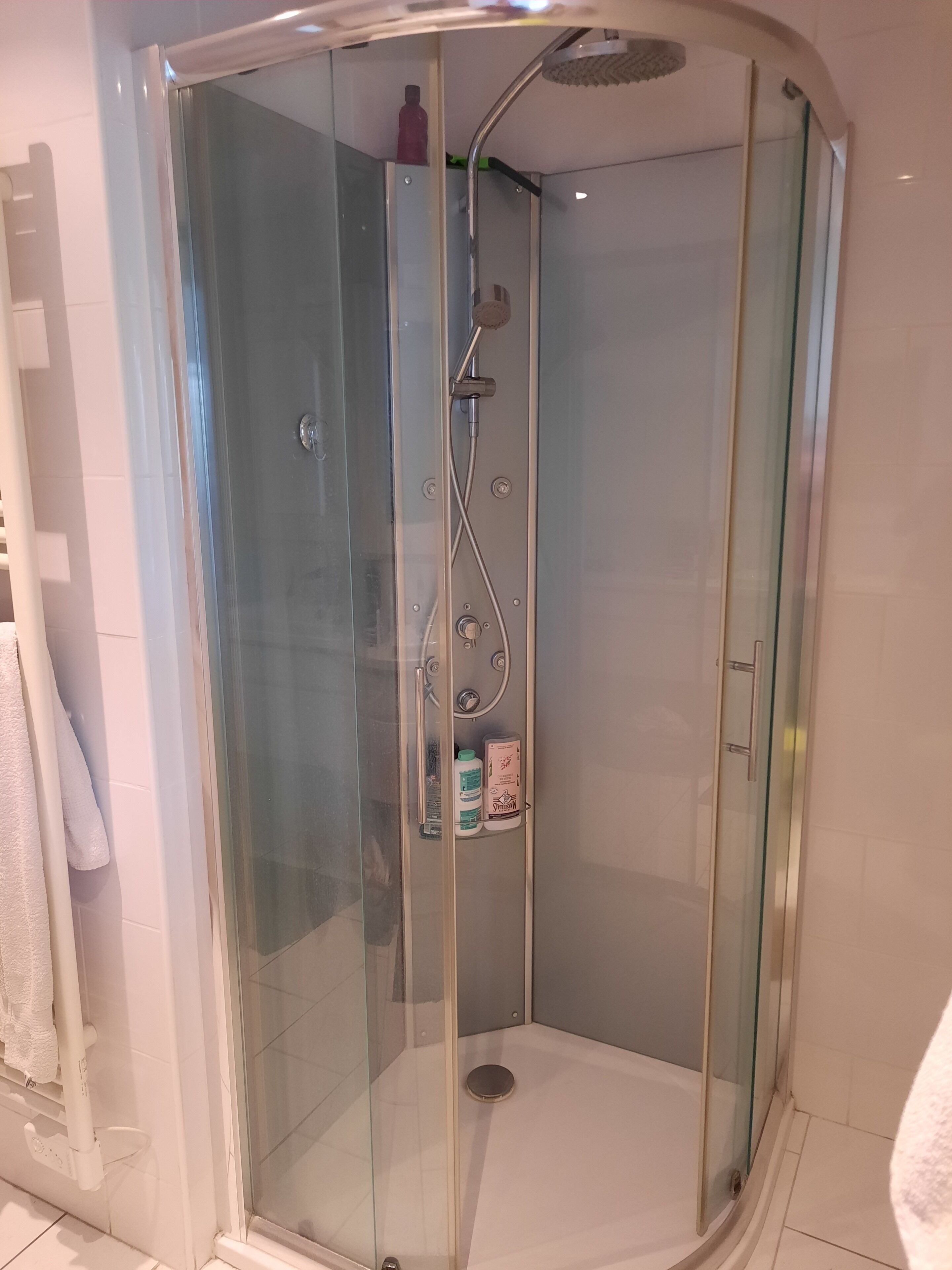 Eine Duschkabine mit Glaswänden, einer Handbrause und einem Shampoo.