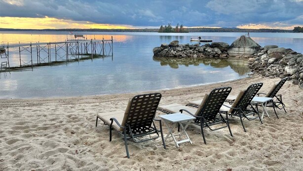 Una playa con sillas de descanso y un muelle que se adentra en aguas tranquilas.