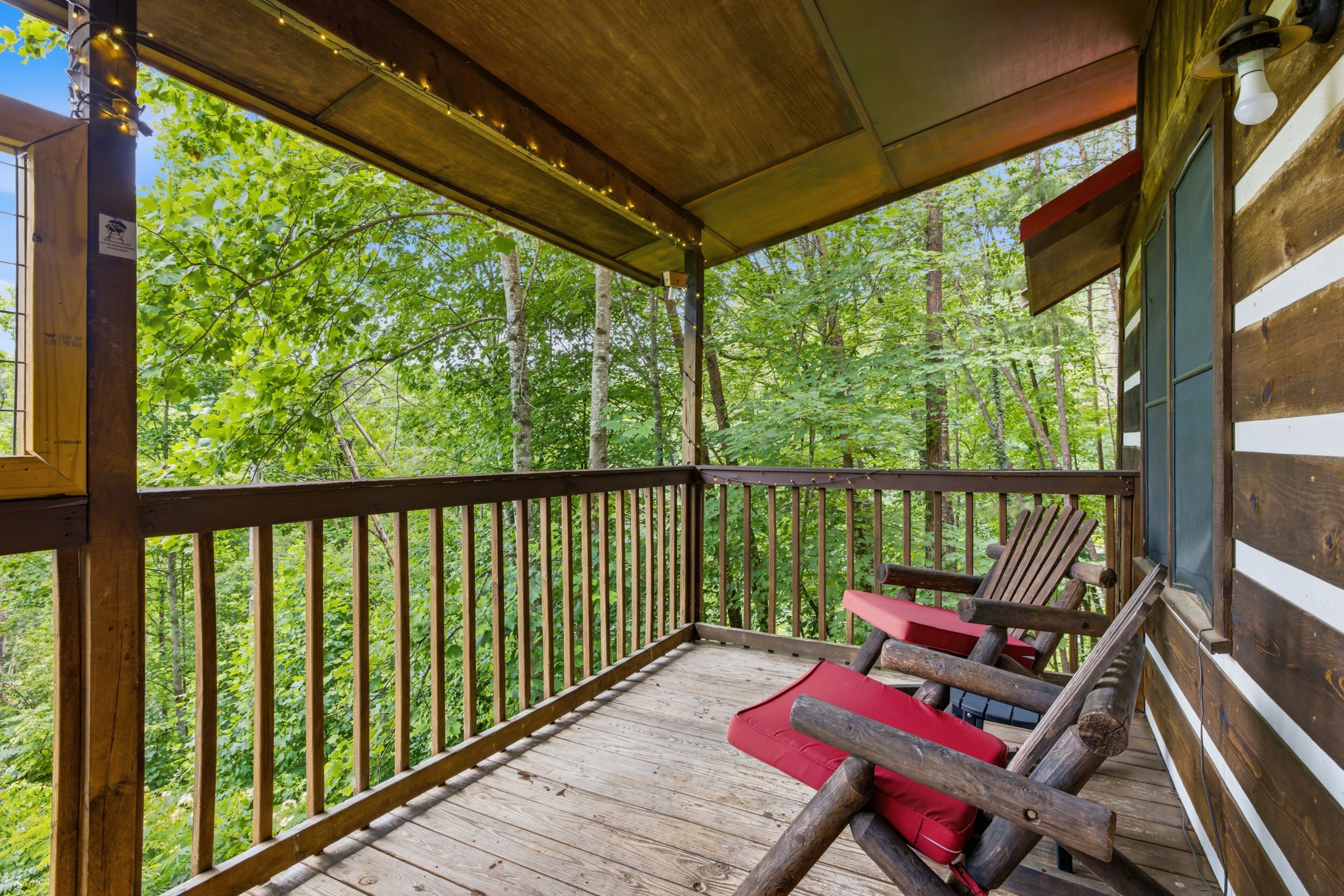 Une terrasse en bois avec une rambarde, des chaises rembourrées rouges et une vue sur une forêt.