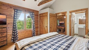 A bedroom with a bed, wooden walls, a window with curtains, a television, and a door leading to another room. - Cedar Ridge Cabin 1 Bedroom Cabin (Sevierville)