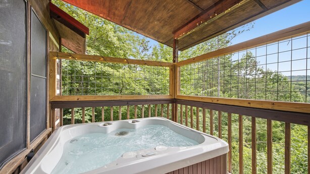 A hot tub in a wooden deck with a view of a forest. - Cedar Ridge Cabin 1 Bedroom Cabin (Sevierville)