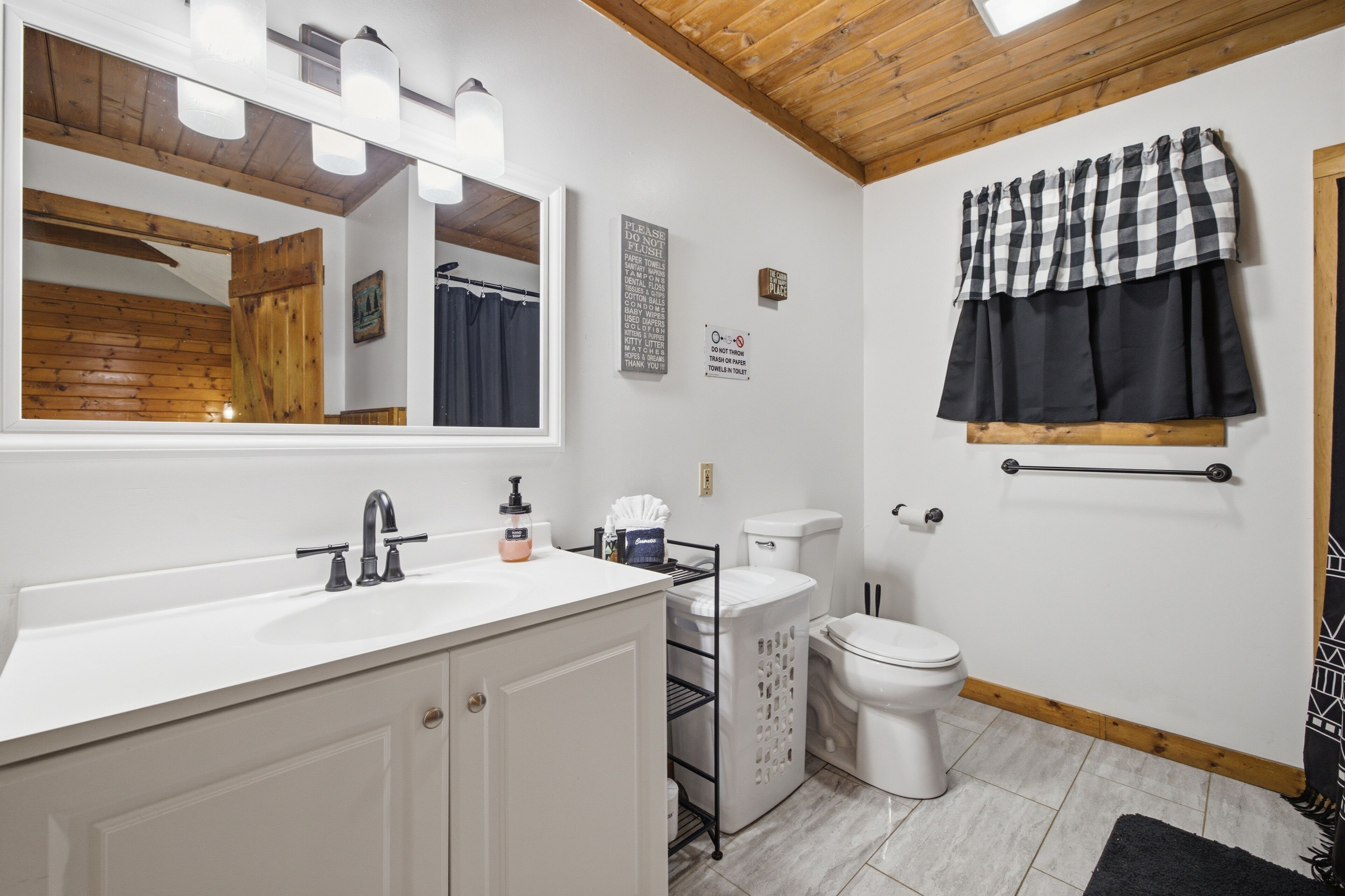 Une salle de bain avec un lavabo blanc, un miroir et des toilettes, un plafond en bois et un tapis noir.