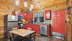 A wooden cabin interior with a kitchen featuring red cabinets, a refrigerator, a stove, and a sink. - Cedar Ridge Cabin 1 Bedroom Cabin (Sevierville)