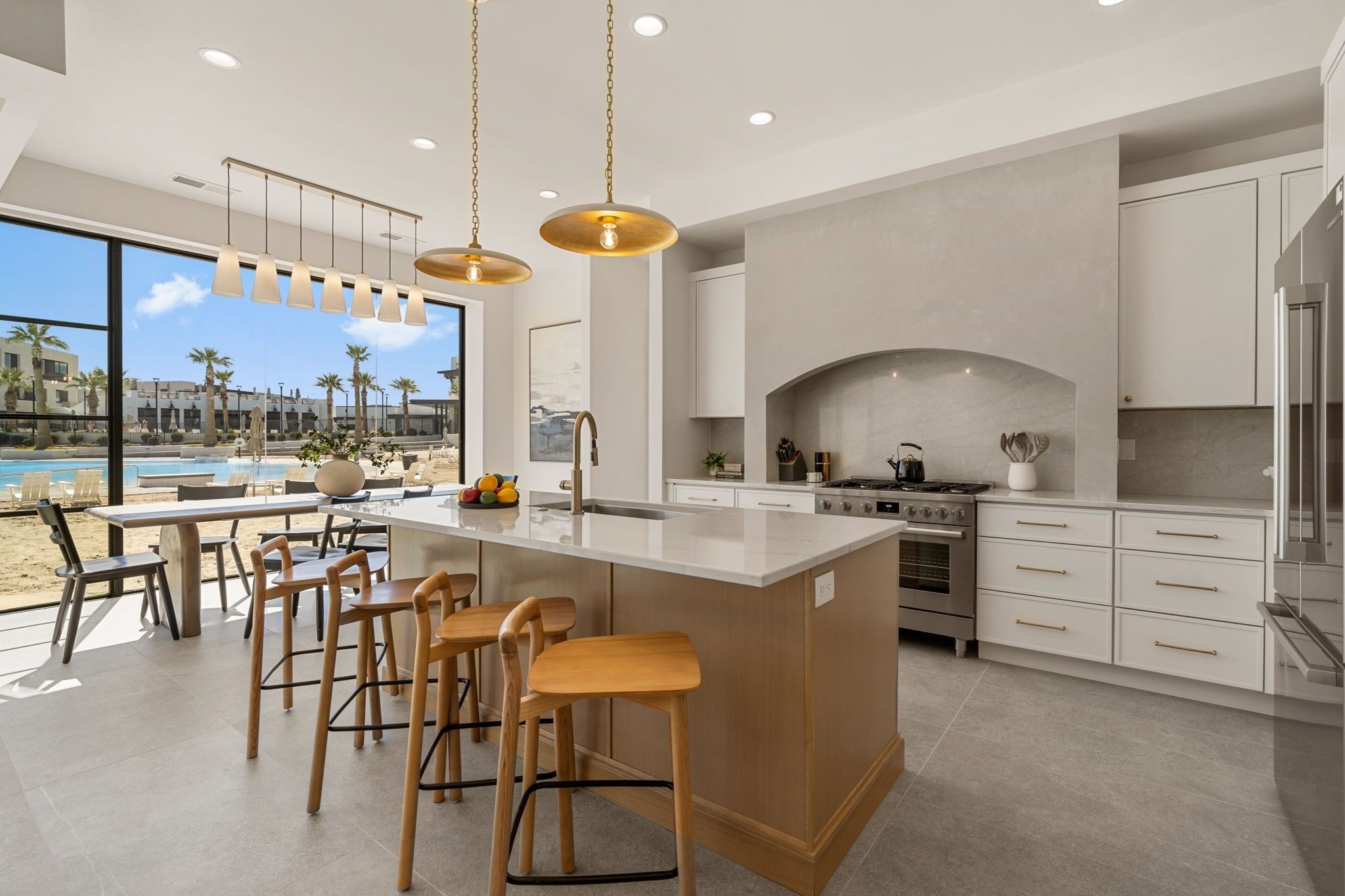 Una cocina moderna con una isla grande, taburetes de bar y vistas a una piscina y palmeras.
