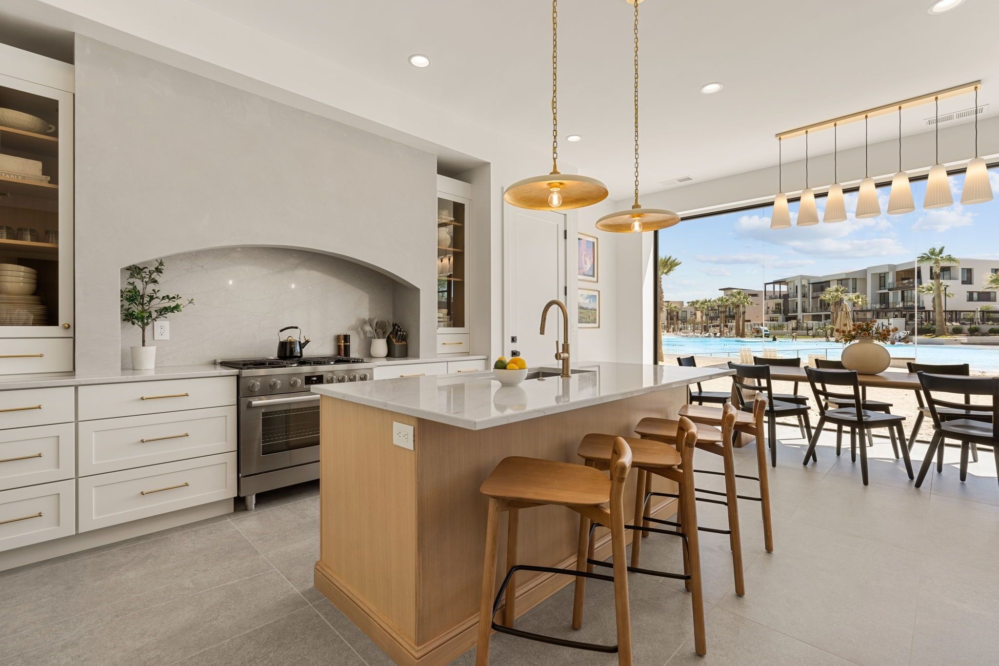 A modern kitchen with a central island, bar stools, and a view of a pool.