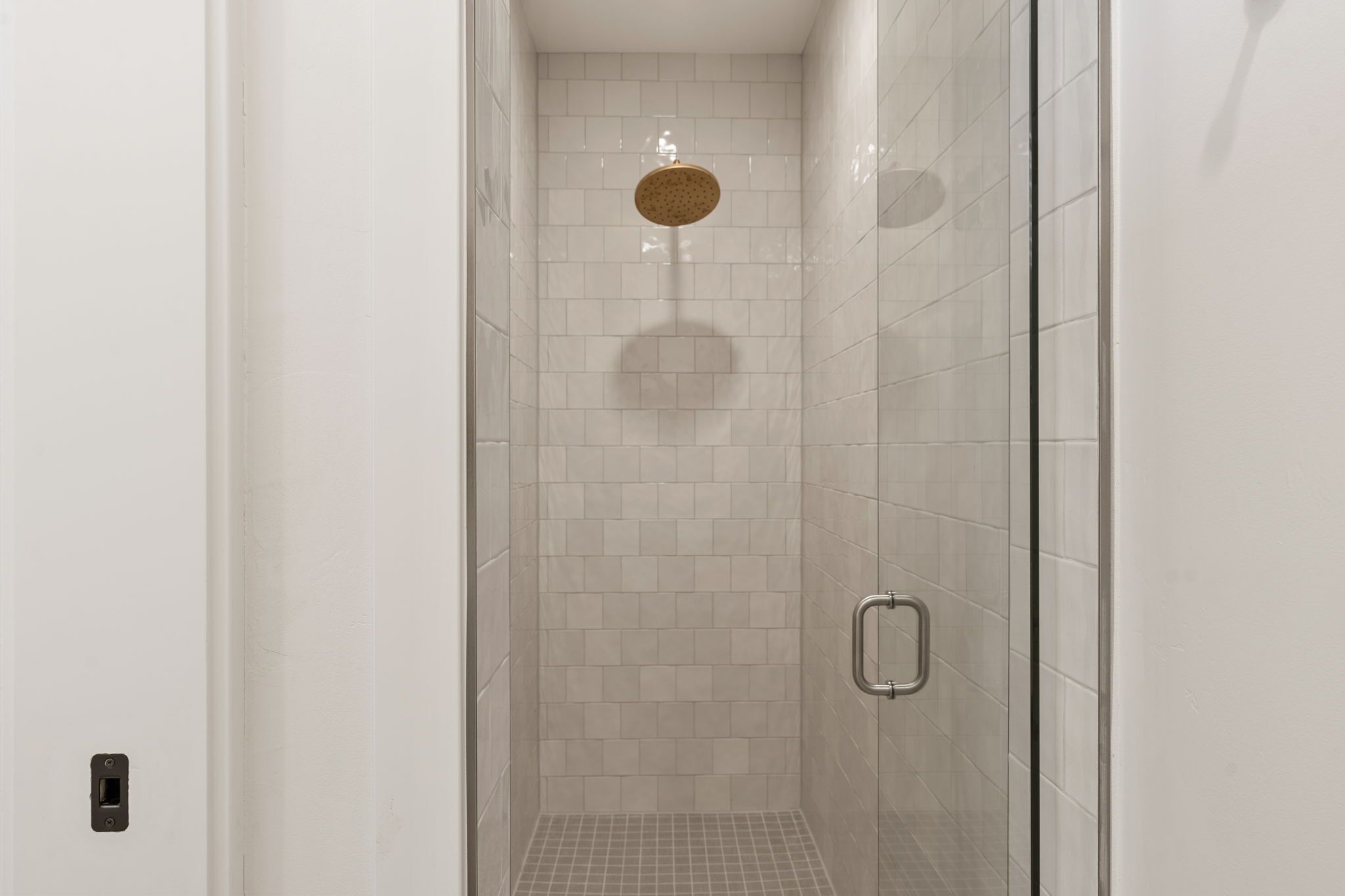 A narrow, tiled shower area with a round, perforated showerhead and a metal handle on the door.
