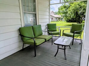 Eine überdachte Veranda mit einem grünen Sofa, zwei Stühlen und einem kleinen Tisch.