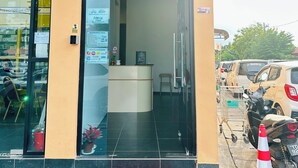 Entrada de un hotel con mostrador de recepción, un tapete con la palabra 'Welcome' y un letrero de farmacia en la parte superior.