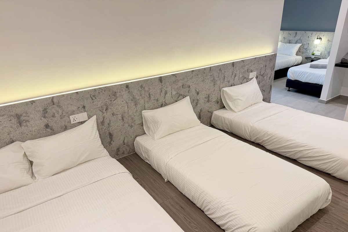 A hotel room with three single beds, a marble headboard, a bedside table with a lamp, and a small plant.