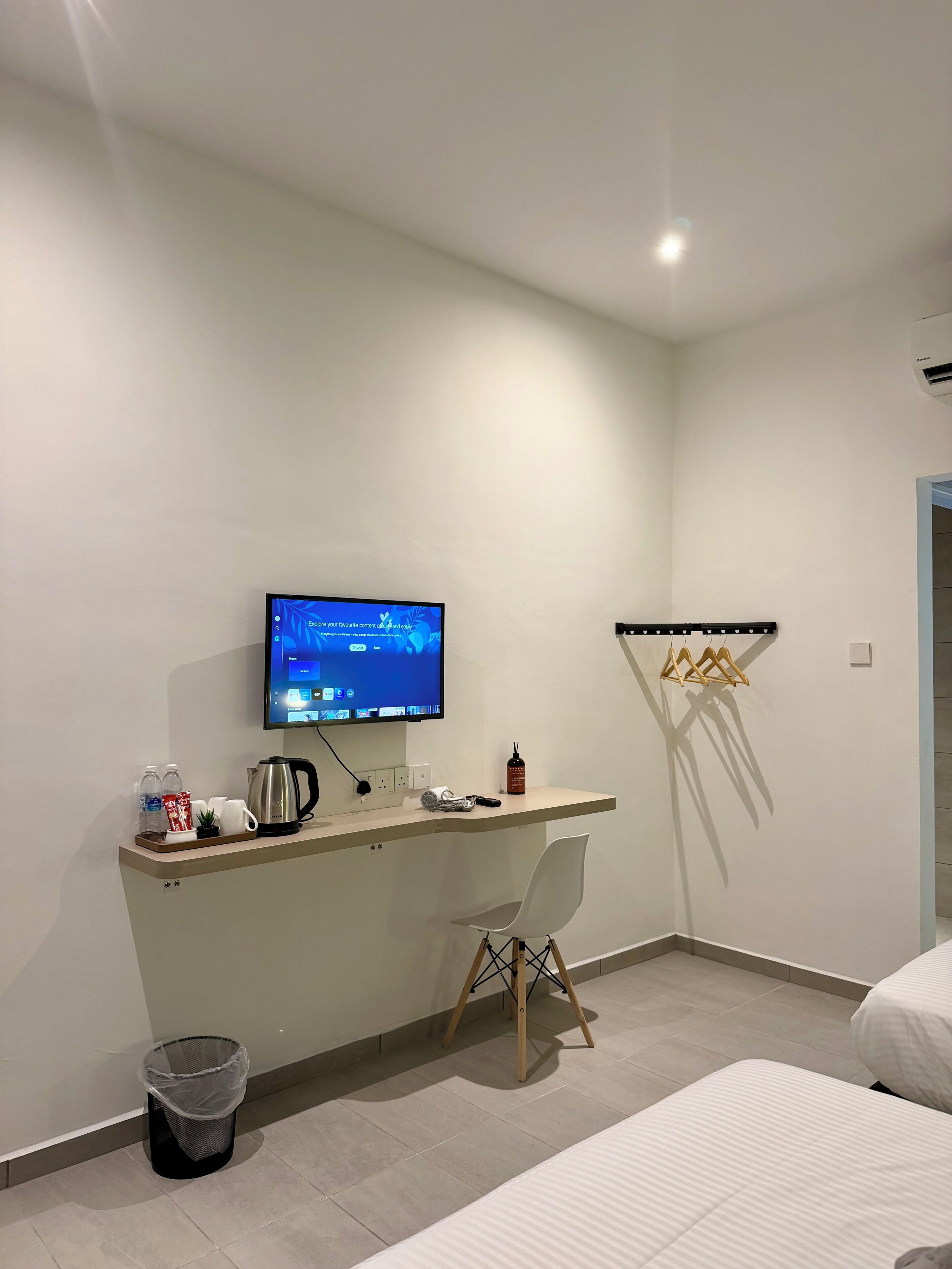 Une chambre d’hôtel moderne équipée d’un bureau, d’un écran d’ordinateur, d’une chaise, d’un lit, d’une poubelle et d’un porte-manteau fixé au mur.
