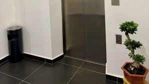 Un ascensor con pantalla digital, un cesto de basura y una planta en maceta.