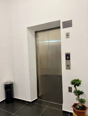 An elevator with a digital display, a trash bin, and a potted plant. - Fat Mom Room & Stay (Langkawi)