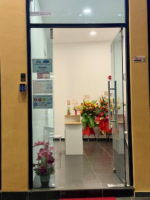 A reception area with a glass door, a desk with a red tablecloth, and a bouquet of flowers. - Fat Mom Room & Stay (Langkawi)
