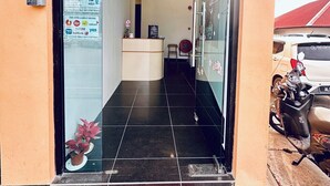 Entrada de un hotel con una recepción, un felpudo rojo y una motocicleta estacionada afuera.
