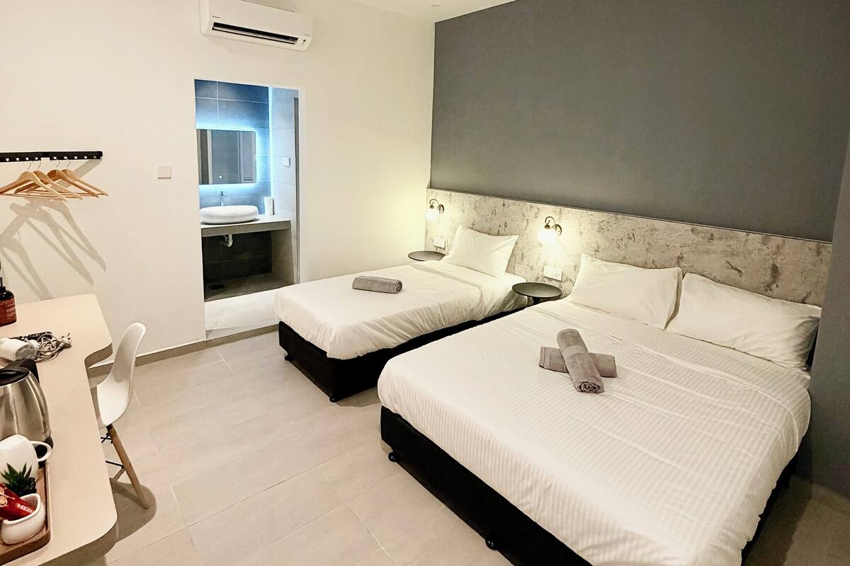 A modern hotel room with two beds, a desk with a chair, and an air conditioning unit.