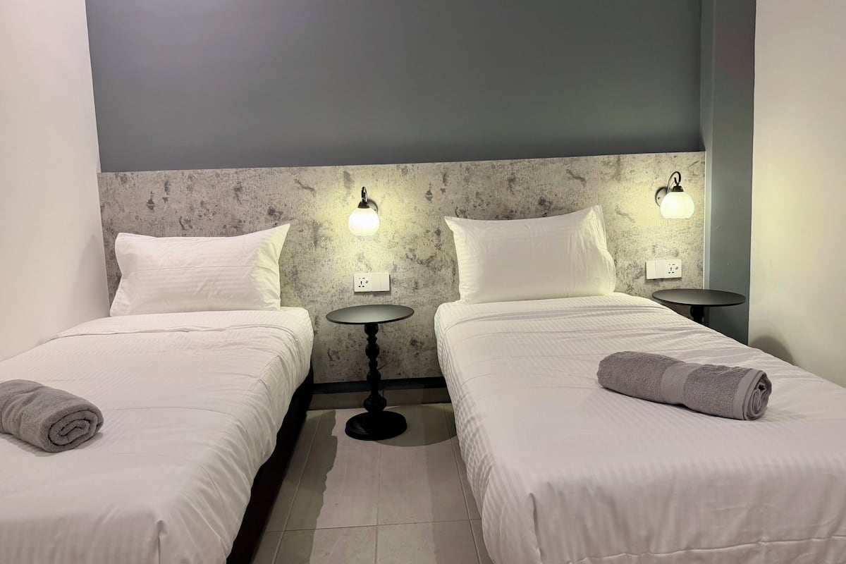A hotel room with two single beds, a round table, and wall-mounted light fixtures.