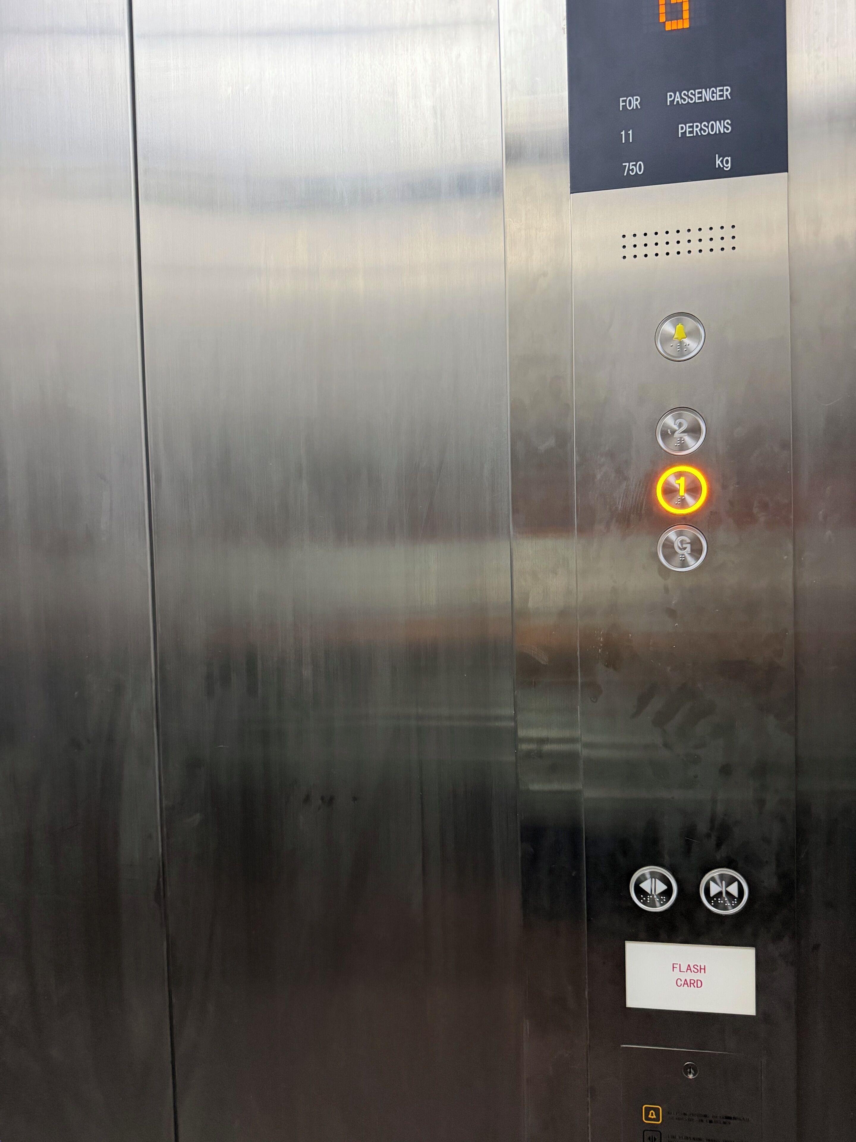 An elevator control panel with a digital display, emergency bell button, floor selection buttons, and a flash card slot.