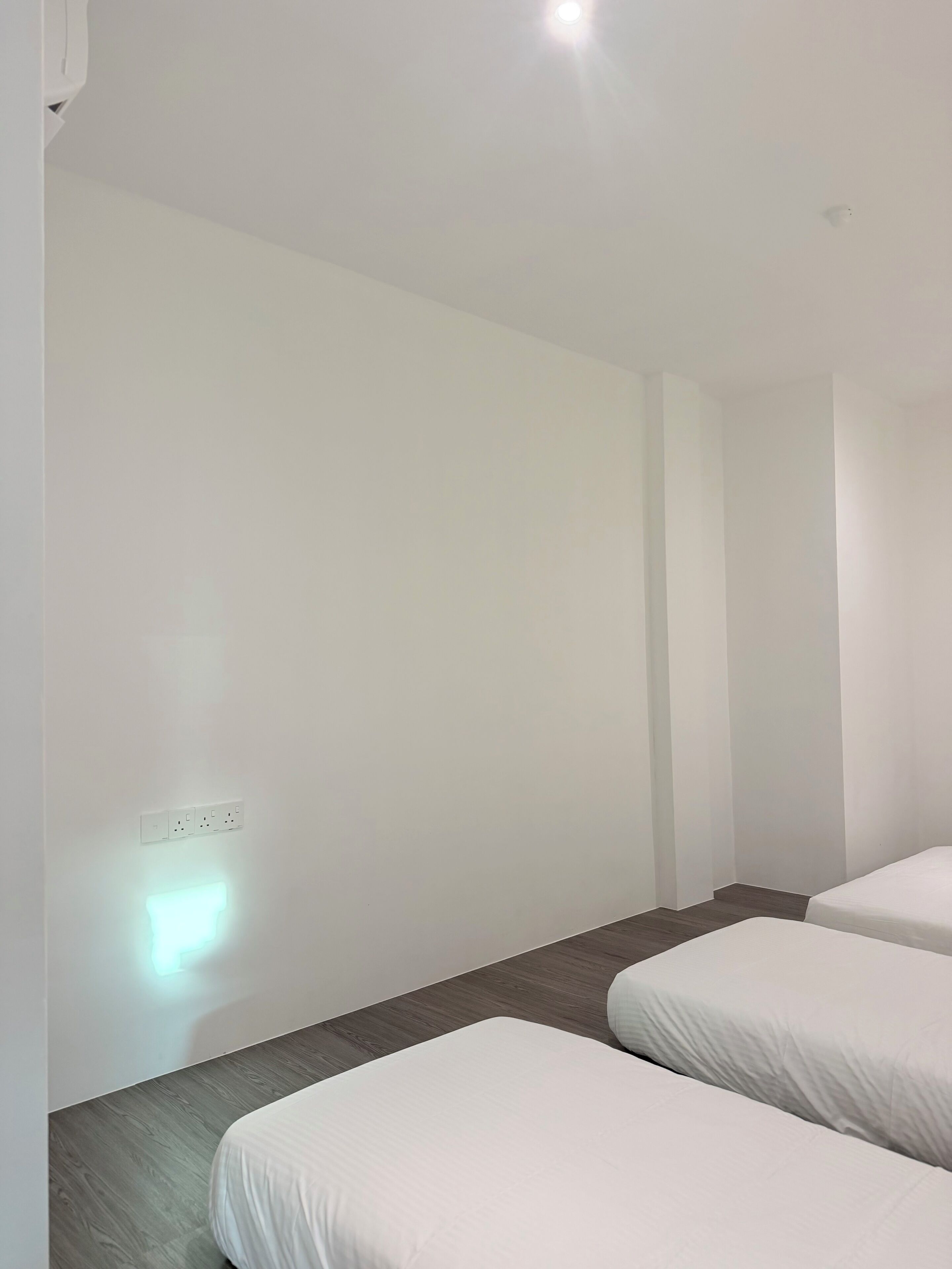 A hotel room with two beds, a wooden floor, a white wall, and a ceiling light.