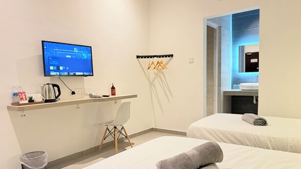 Una habitación de hotel con escritorio, televisor, dos camas, baño y un cubo de basura.
