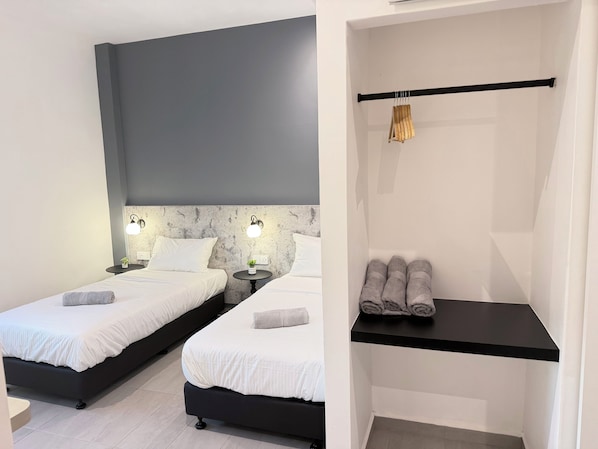 Un dormitorio moderno con dos camas, una mesita de noche pequeña con lámpara y un perchero para toallas.