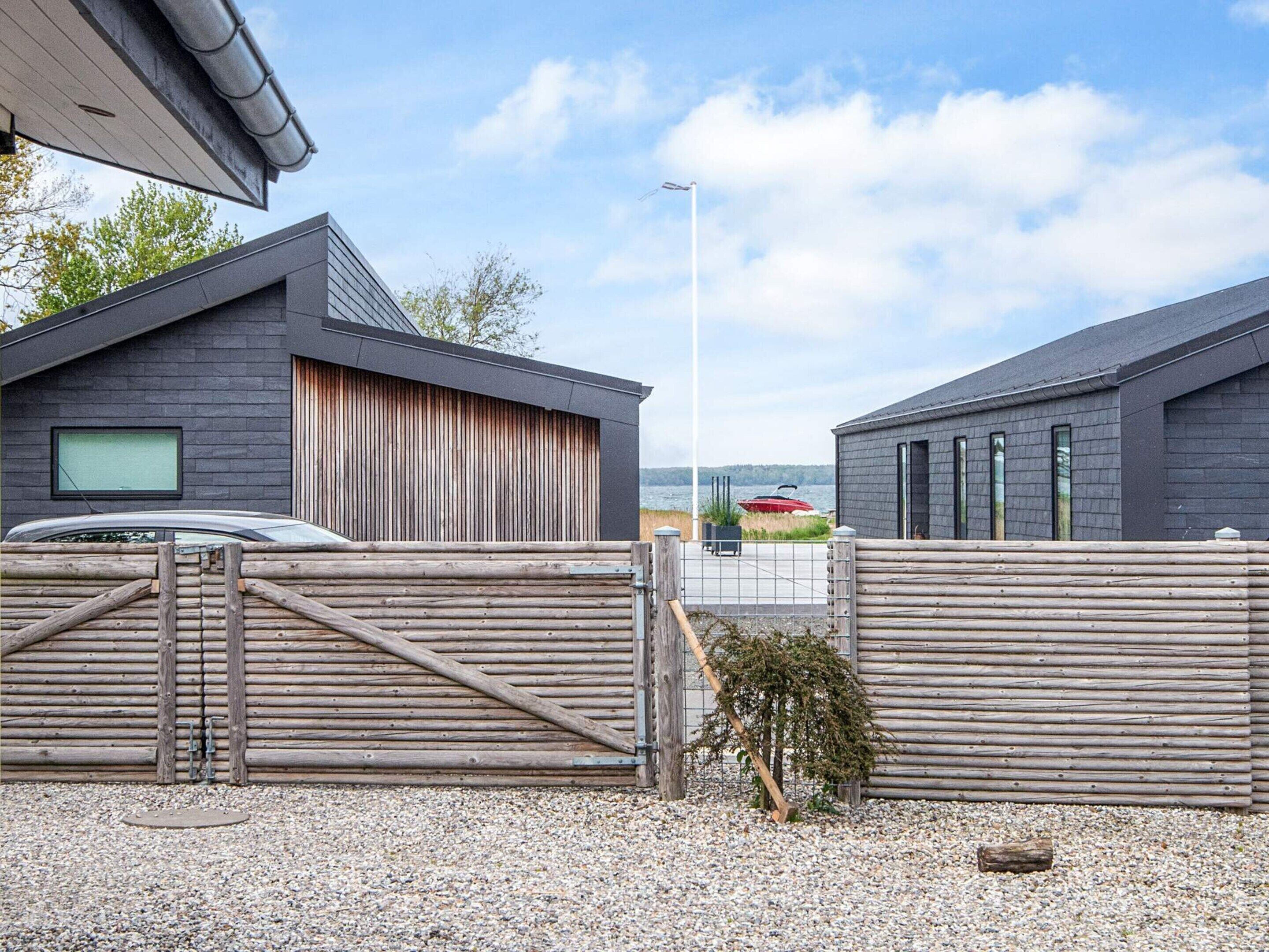 A modern building with a wooden fence, a car, and a boat in the background.