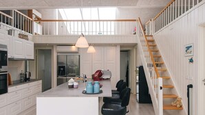 Una cocina moderna con una isla central, taburetes de bar, una escalera y vistas al área de estar.