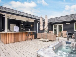 Eine Holzterrasse mit Whirlpool, Sitzgelegenheiten im Freien und einer Bar.