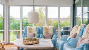 Una sala de estar moderna con ventanas amplias, muebles de mimbre y una lámpara colgante.