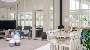 Amplia sala de estar con una gran mesa de comedor, sillas blancas, chimenea y televisión.