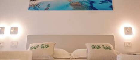 A bedroom with a bed, two pillows with green designs, a wall-mounted picture of a beach, and bedside lamps.
