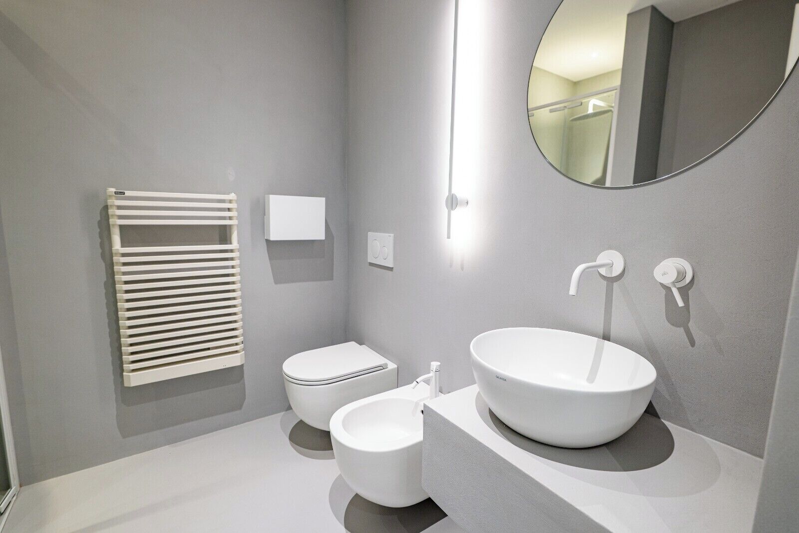 A modern bathroom with a toilet, bidet, and a large round sink.