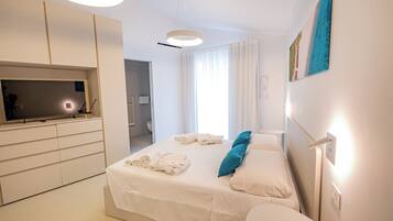 Una habitación de hotel moderna con cama, televisor, escritorio y baño visible a través de una puerta abierta.