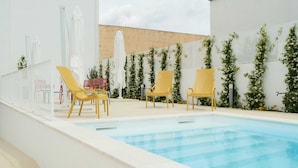 A pool area with yellow lounge chairs, white umbrellas, and climbing plants.