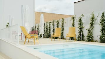 Una piscina al aire libre, sombrillas, sillones reclinables de piscina